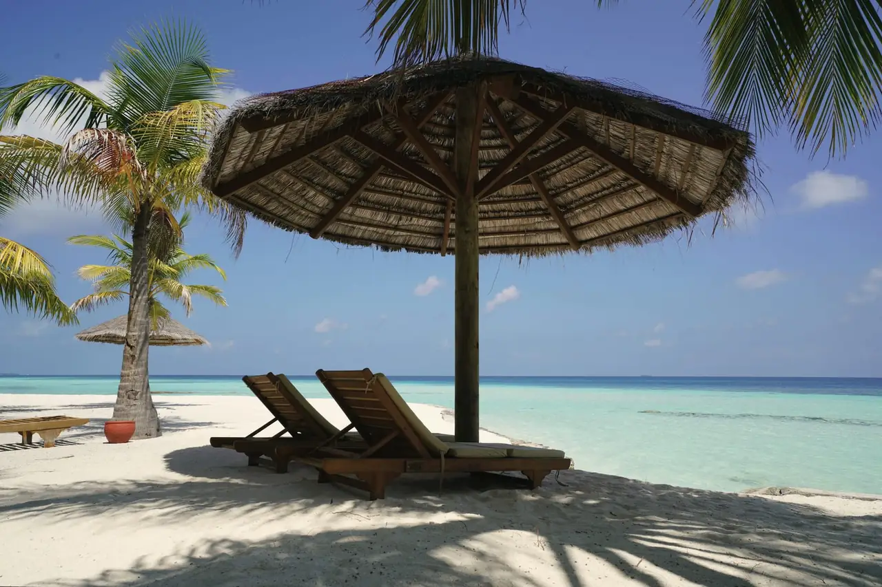 Two timber loungers under a thatched shade on white sand