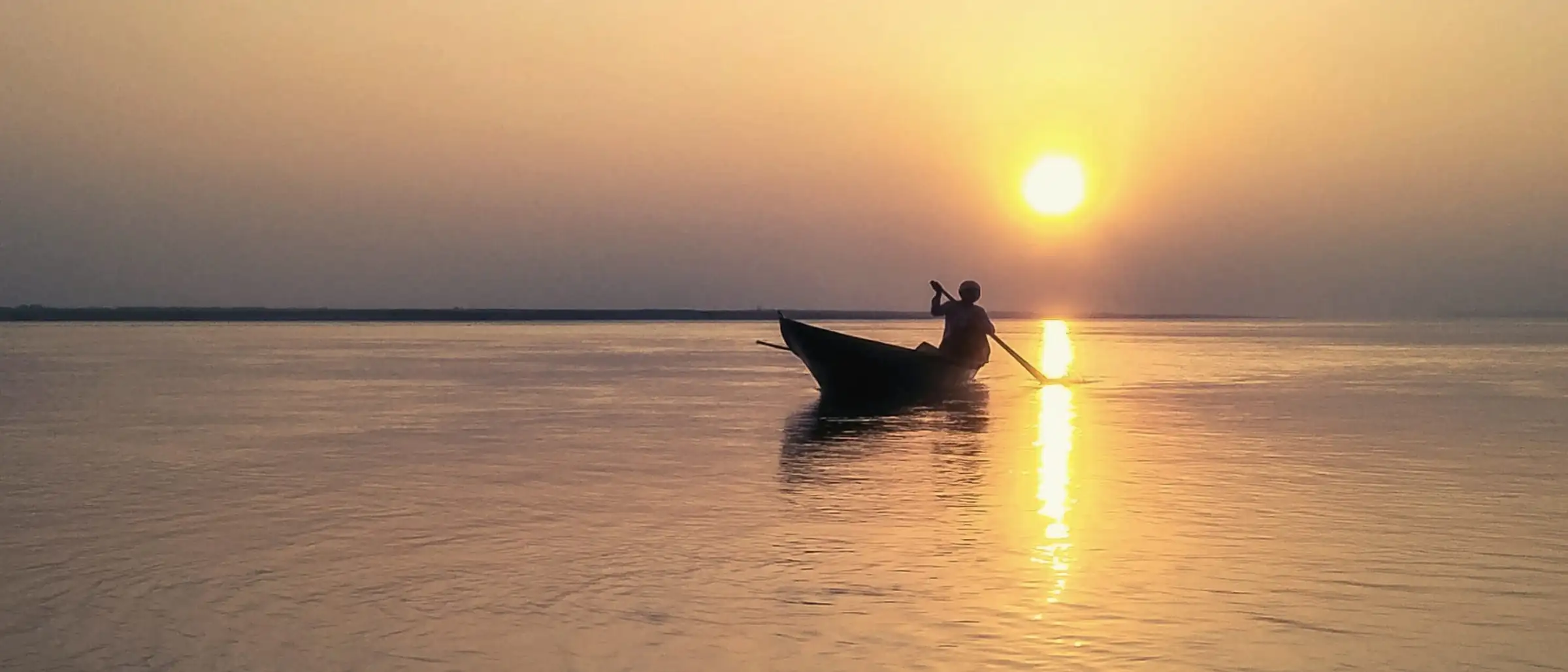 A wooden boat on still water as the sun sets over the lagoon