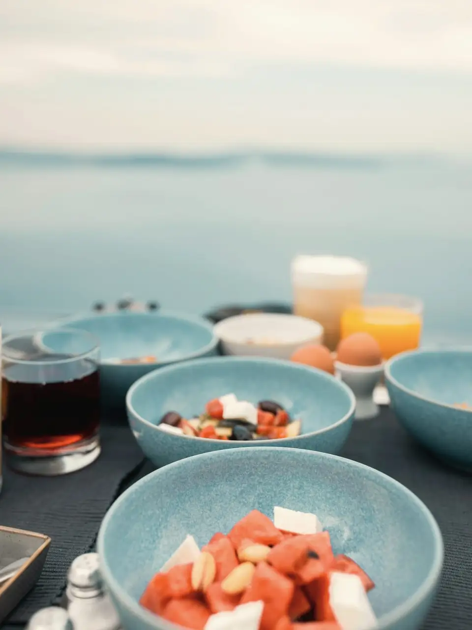Bowls of watermelon, yoghurt and fruit on a terrace table, with juice and the sea behind