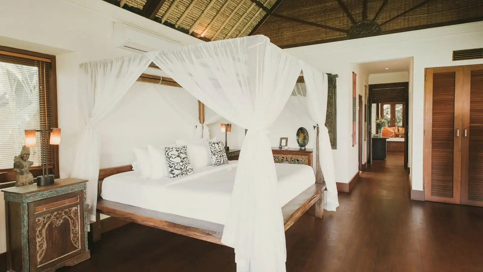 Canopy bed with white netting under a high pitched timber ceiling