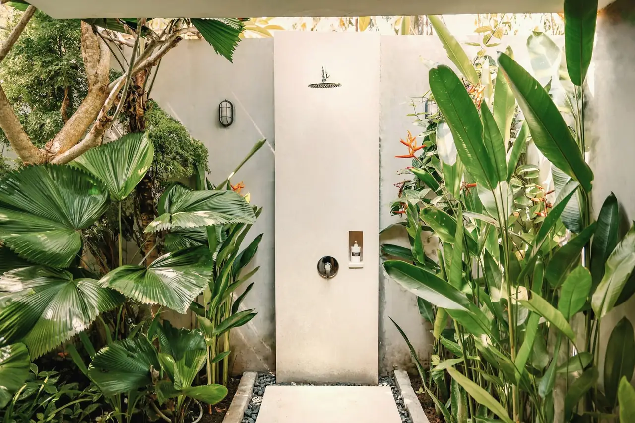 Outdoor rain shower against a white wall, surrounded by tropical plants