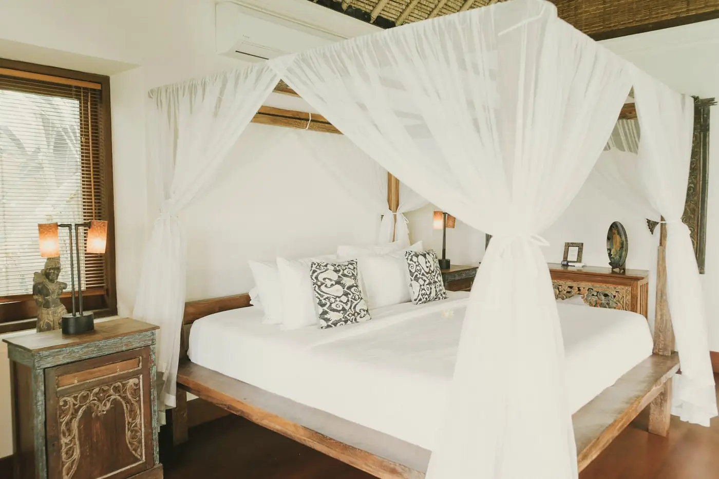 Canopy bed with white netting and a carved timber bedside table