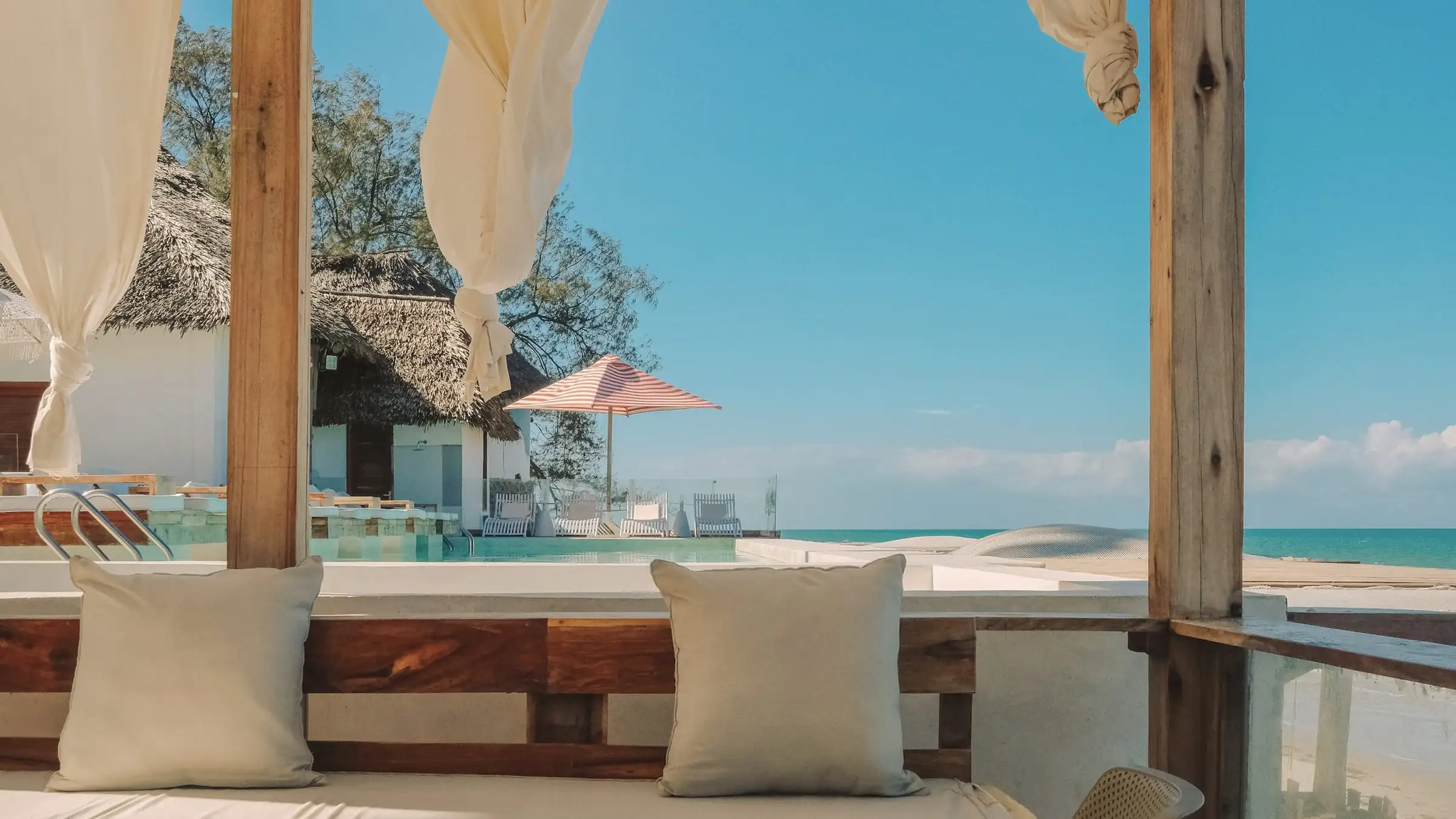 Canopy daybed on a terrace, its linen curtains framing a turquoise lagoon