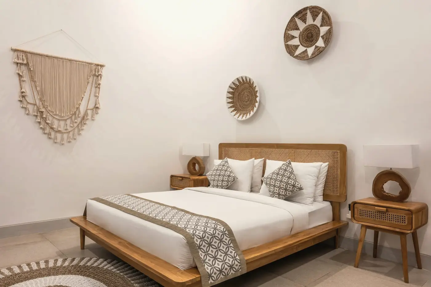 Whitewashed bedroom with a low timber bed, linen bedding and woven wall hangings