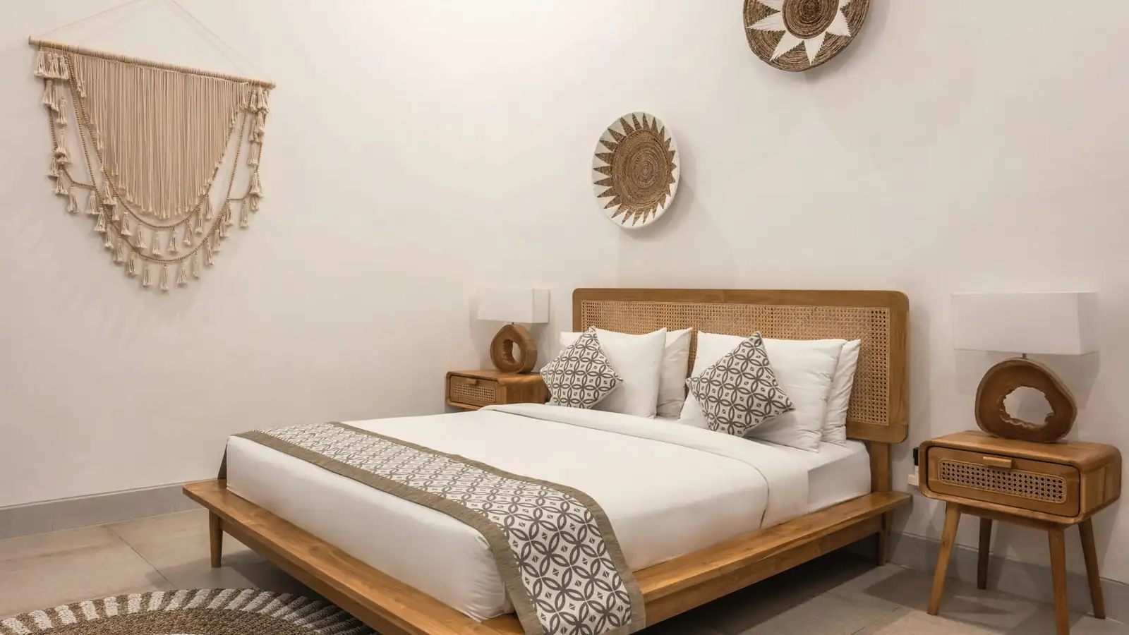 Whitewashed bedroom with a low timber bed, linen bedding and woven wall hangings