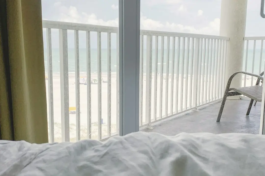 Unmade linen bed facing an open balcony door and the sea