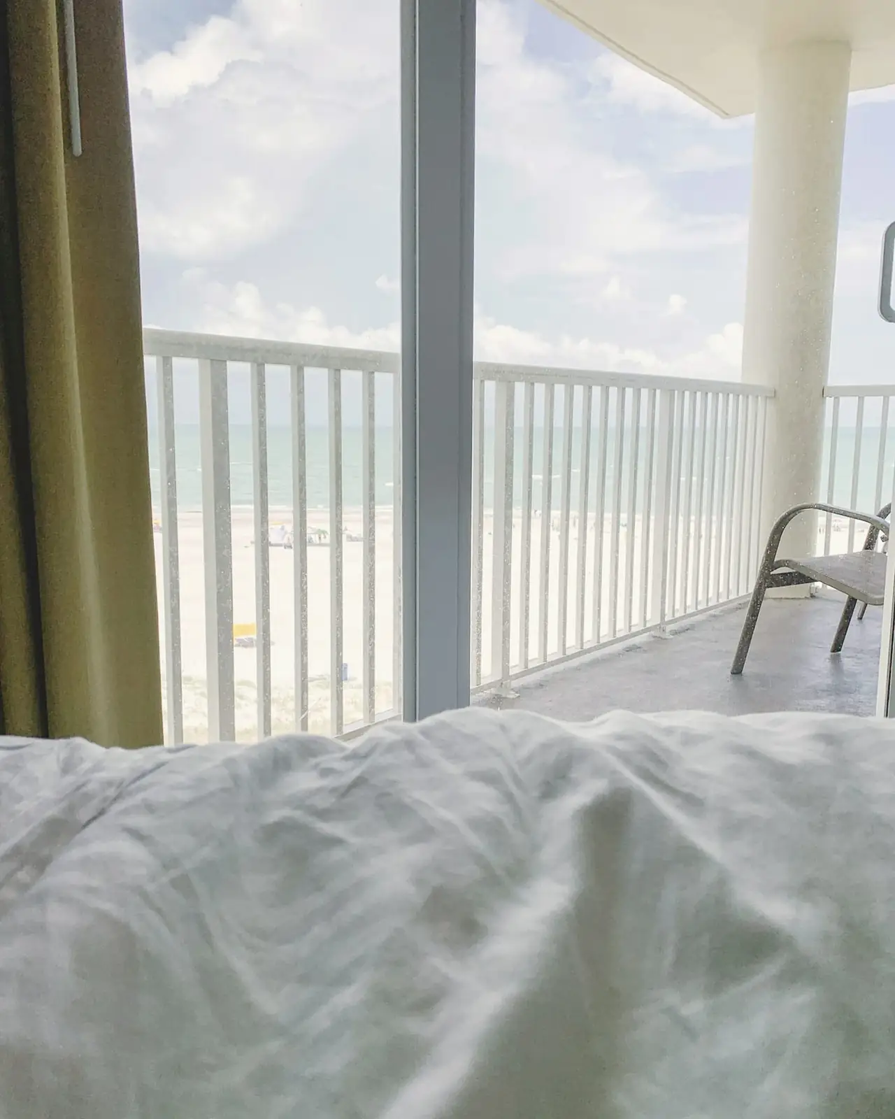 Unmade linen bed facing an open balcony door and the sea