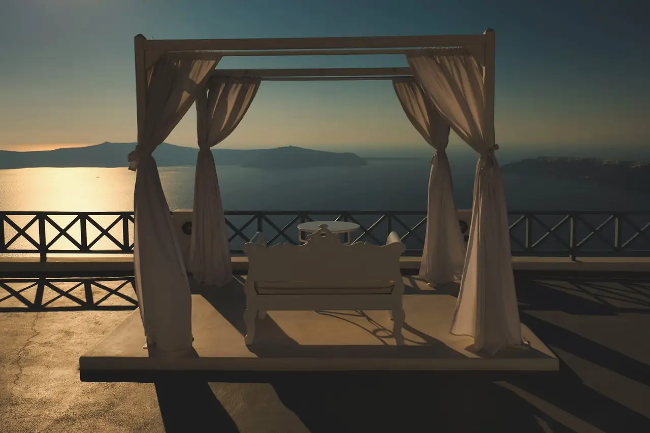 Canopy daybed with white curtains on a terrace at sunset