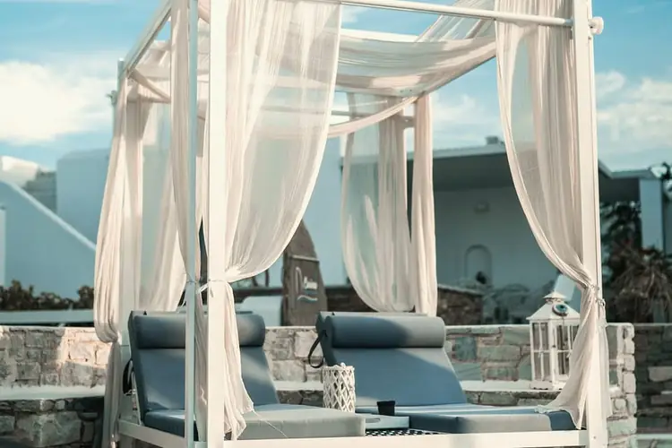 Canopy daybed with white curtains on a stone terrace under a blue sky