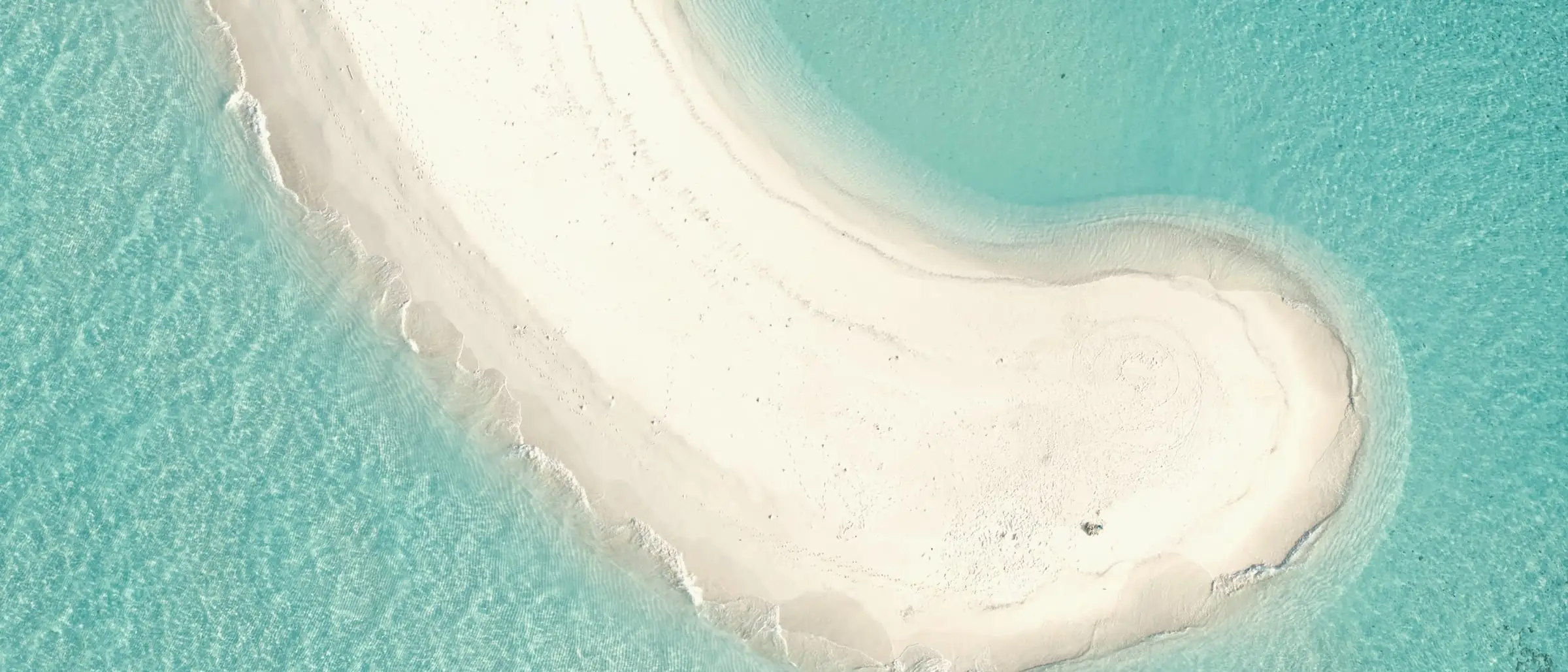 A curved white sandbank in a turquoise lagoon, seen from above