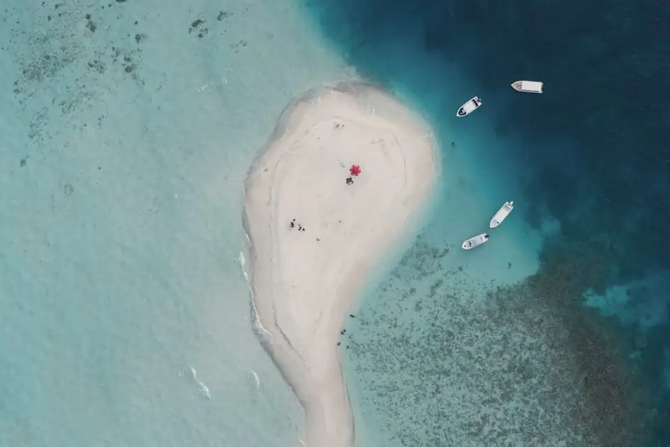 Curved white sandbank in turquoise water, seen from above, with a boat moored nearby