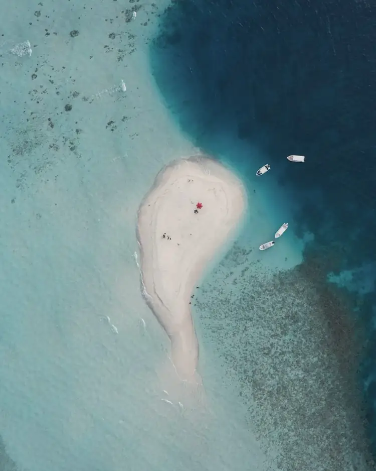 Curved white sandbank in turquoise water, seen from above, with a boat moored nearby