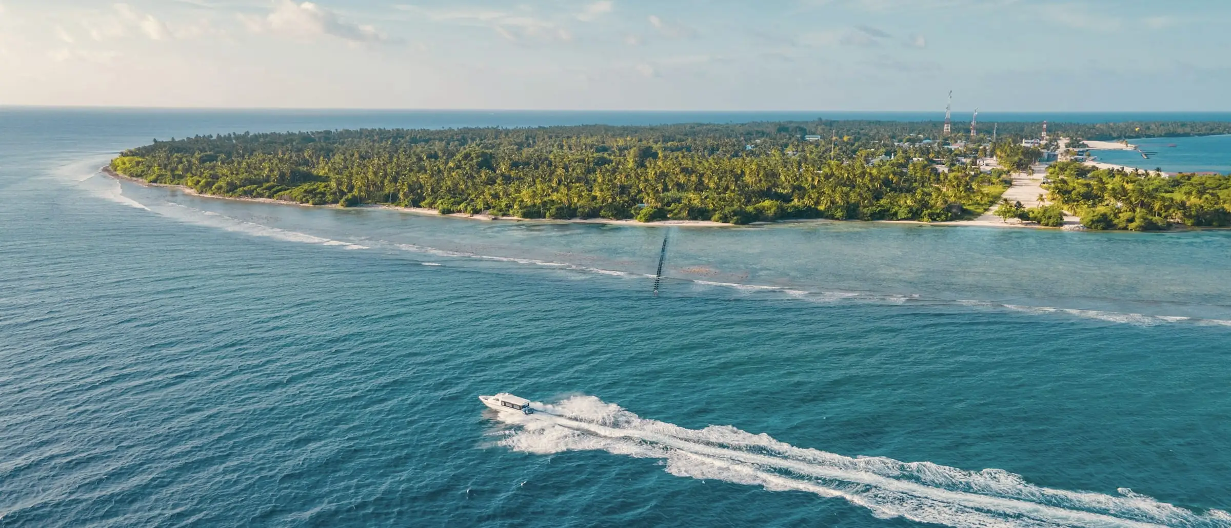 A speedboat crossing open water towards a palm-covered island